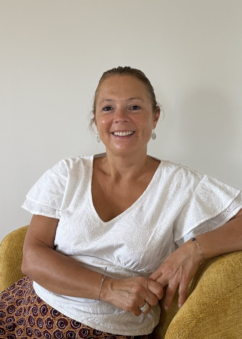 Céline Olmi, psychopraticienne, assise dans un fauteuil de son cabinet, souriante.